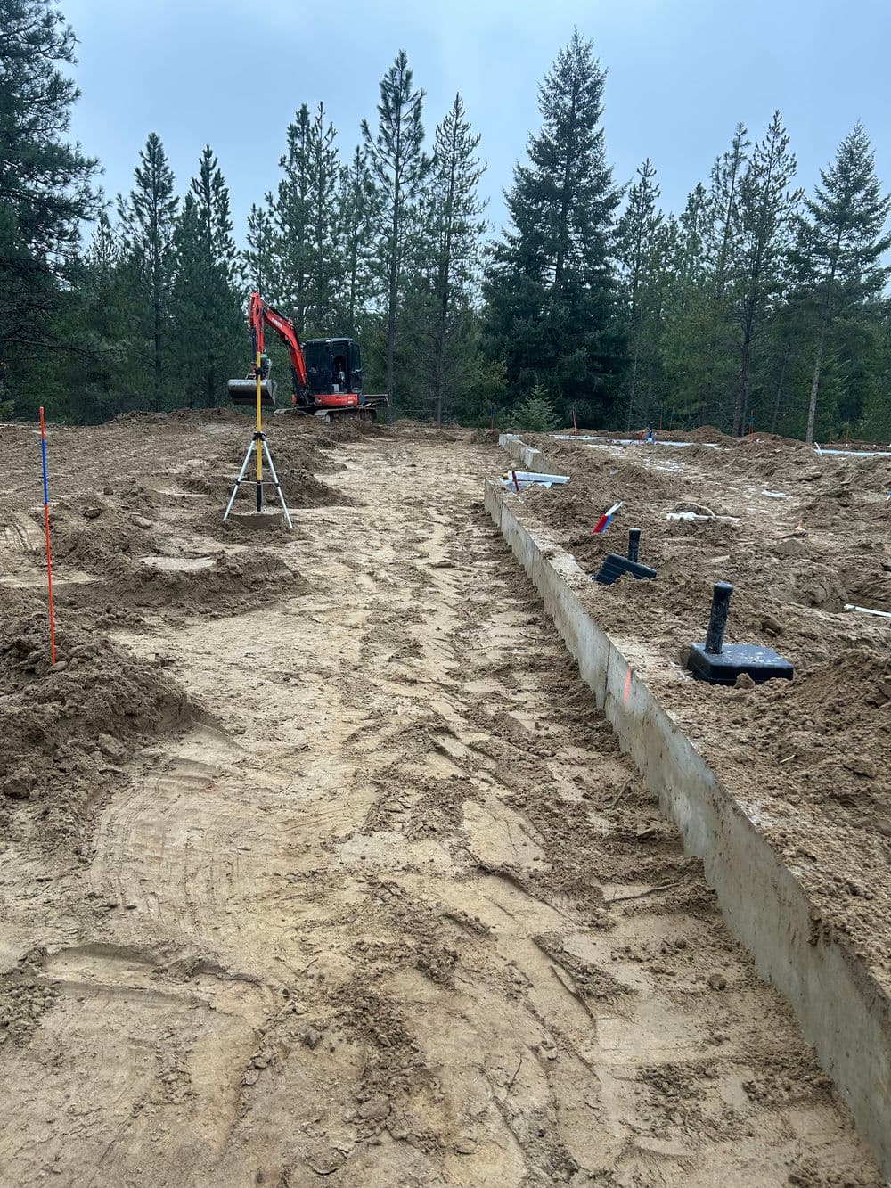 Construction site with excavated foundation and equipment in a forested area.