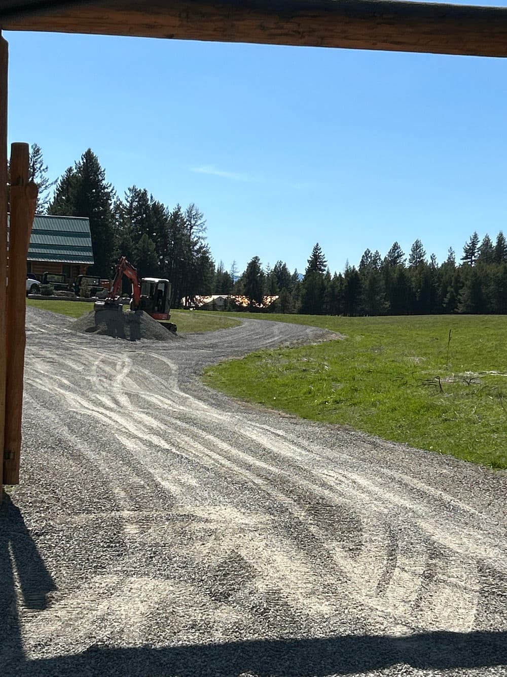 Gravel driveway leading to construction site surrounded by trees and clear blue sky.