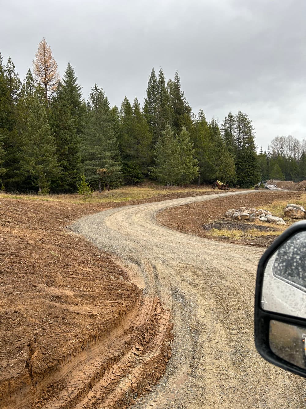 Gravel road winding through a forested area with trees and cloudy sky.